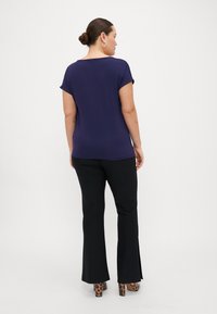 Top de manga corta en color azul marino combinado con pantalones negros de campana, que presentan aberturas laterales y un detalle de tacón con patrón. Tela suave y elástica con un ajuste holgado.