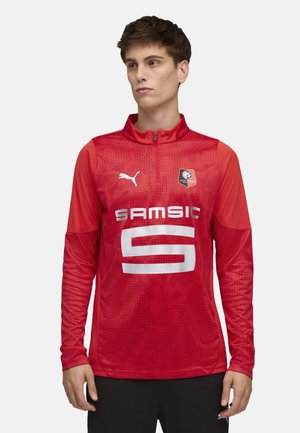 Rød atletisk langærmet top med halvlukning, der har et struktureret stof, hvide logo-accenter og et fremtrædende "SAMSIC" grafisk print.