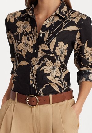 Schwarzes Hemd mit Knöpfen und beigem Blumenmuster, die Ärmel bis zu den Ellbogen hochgekrempelt, in beige hoch taillierte Hose mit braunem Gürtel und runder Schnalle gesteckt.