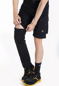 Shorts cargo noirs avec jambes inférieures détachables, comportant plusieurs poches et une coupe légèrement ample. Portés avec des baskets noires et jaunes.