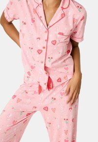 Lichtroze Pyjama-set met korte mouwen, met contrasterende rode afwerking. Patroon bevat tijgers, harten, bloemen en sterren. Zachte stof.