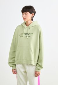 Lys grønn hettegenser laget av mykt materiale, med kenguru-lomme, snorhette og trykt logo på brystet.
