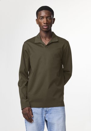 Long-sleeve, olive-green polo shirt with a collar. Features a relaxed fit and soft texture, paired with light blue denim jeans.