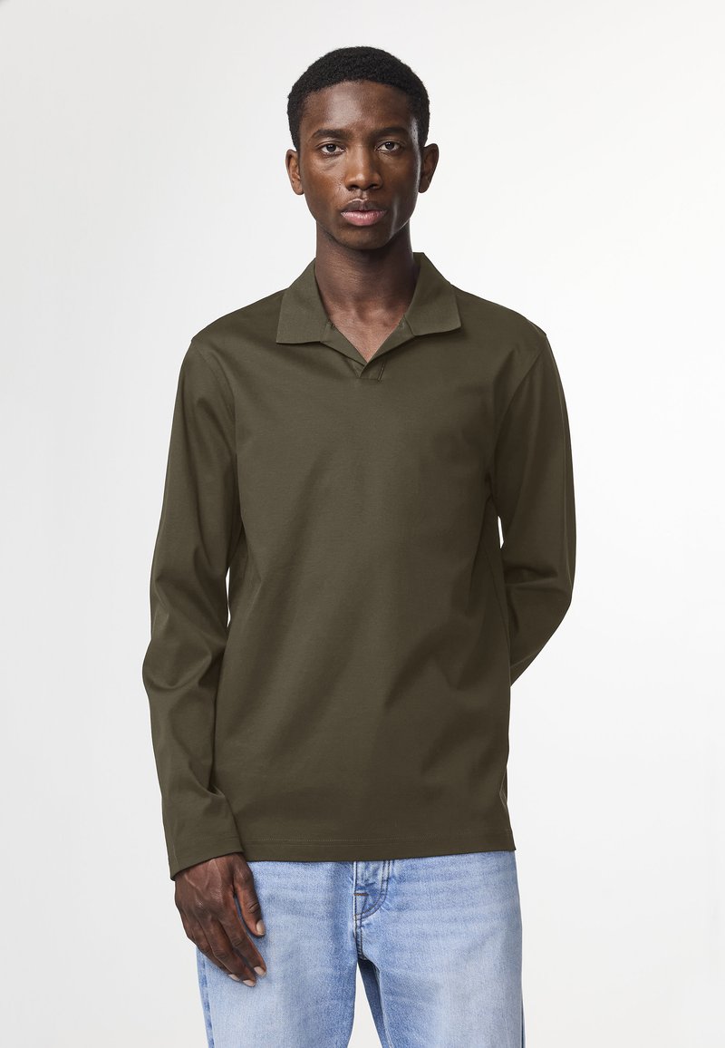 Long-sleeve, olive-green polo shirt with a collar. Features a relaxed fit and soft texture, paired with light blue denim jeans.