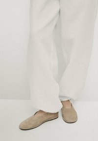 Beige suède instapschoenen met een ronde neus en minimale stiksels, gedragen met witte, loszittende broeken. Vriendelijke textuur, eenvoudig ontwerp.