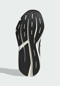 Čierna guma podrážky topánky so vzorom textúrovaného behúňa, drážkami a bielymi akcentmi na stranách. Kontúrovaný tvar pre vylepšenú trakciu.