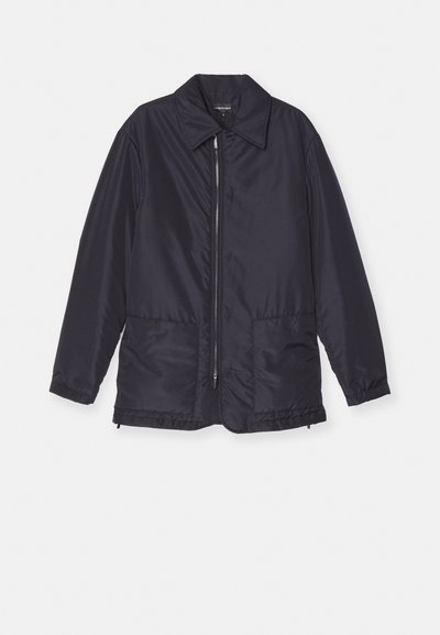 Casaco acolchoado azul marinho, leve, com fecho frontal, dois bolsos frontais e colarinho. Textura suave, punhos e bainha elásticos.