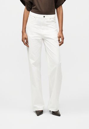 Γυναίκα που φοράει λευκό παντελόνι με ψηλή μέση και φαρδύ πόδι, συνδυασμένο με σκούρο κοντομάνικο τοπ και μαύρα πέδιλα με μυτερή μύτη.