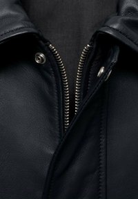 Schwarze Lederjacke mit silbernem Reißverschluss, Druckknopfverschluss und strukturiertem Material mit sichtbaren Nähten entlang der Kanten.