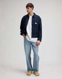 Τζιν μπουφάν σε σκούρο μπλε με τσέπη μπροστά, φορεμένο πάνω από λευκό μπλουζάκι. Συνδυασμένο με ανοιχτό μπλε τζιν παντελόνι και μπεζ παπούτσια slip-on.