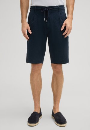 Shorts bleu marine en tissu texturé, avec taille élastique et cordon de serrage. Présente deux poches latérales et une coupe droite. Associés à des chaussures noires à enfiler.