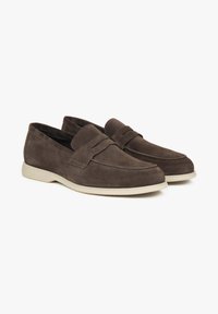 Bruine suède instappers met een slip-on ontwerp, contrasterende lichte rubberen zolen en een decoratieve band over de bovenkant.