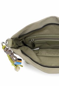 Wnętrze zielonej tkaninowej torebki z zapinaną na suwak kieszonką, kontrastującym przeszyciem oraz dekoracyjnym zawieszką przypiętą do suwaka.