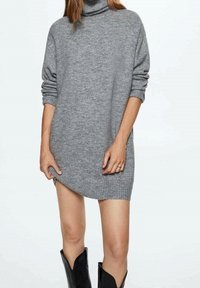 Szary, oversize sweter z golfem, z podwiniętymi rękawami, o miękkiej fakturze i asymetrycznym wykończeniu dołu, zestawiony z czarnymi kozaczkami sięgającymi kolan.