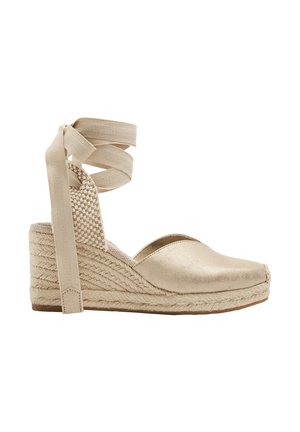 Beżowa espadryla na klinie z zamkniętym noskiem, plecioną podeszwą z juty i sznurowaniem wokół kostki, pokazana z profilu na białym tle.