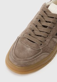 Baskets en daim marron avec un bout arrondi, une tige texturée et des lacets assortis. Elles présentent une semelle en caoutchouc avec un bord contrasté en beige et des coutures discrètes.