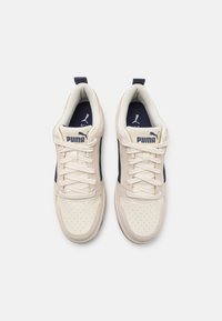 Paire de baskets Puma crème et bleu marine avec lacets noués, vue de dessus sur fond blanc.