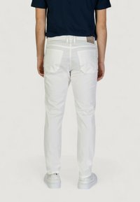 Pantaloni bianchi a gamba affusolata con una texture liscia, dotati di tasche posteriori piatte, una cucitura discreta e un'etichetta in pelle con marchio sulla vita.