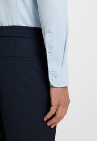 Hellblaues strukturiertes Hemd mit geknöpften Manschetten, kombiniert mit dunkelblauen Hosen mit einer Tasche und dezenter Markenkennzeichnung.