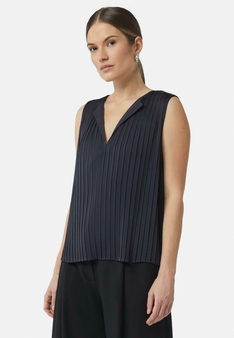 Top senza maniche di colore navy con pieghe verticali, scollatura a V, texture morbida e vestibilità ampia. Indossato con pantaloni neri, design minimalista.