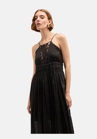 Czarna maxi sukienka wykonana z lekkiego materiału, z koronkowym gorsetem, cienkimi ramiączkami i plisowaną spódnicą, która tworzy zwiewną sylwetkę.