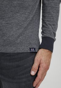 Tricou cu mânecă lungă gri melanj, cu manșetă bleumarin. Are o etichetă din țesătură la margine cu textul "FQ1924 ORIGINAL".