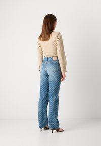Pantalones de mezclilla azul de campana con patrones de texto diagonales blancos, de cintura alta con un parche beige, combinados con una camiseta ajustada de manga larga beige.