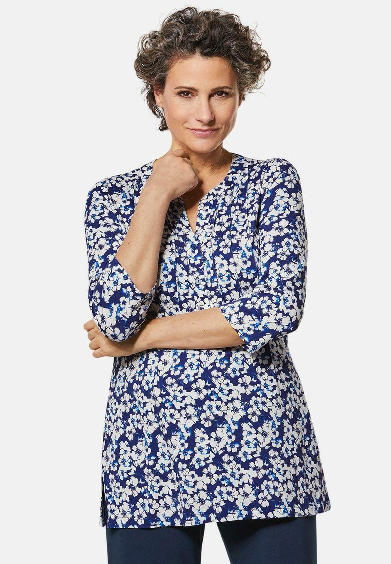 Blumen-Tunika in Marineblau mit weißen und hellblauen Blumen, V-Ausschnitt, dreiviertel Ärmel und einem lockeren Schnitt mit seitlichen Schlitzen.