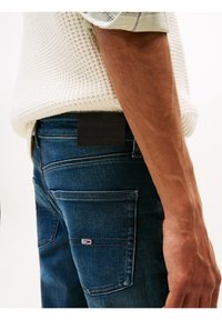 Dunkelblaue Jeans im Slim-Fit, mit einem schwarzen Lederlogo mit der Aufschrift "TOMMY JEANS" und einem kleinen Logo auf der Gesäßtasche.