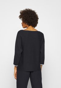 Schwarzer Pullover mit weitem Ausschnitt, Dreiviertelärmeln und kontrastierenden grauen Akzenten an den Bündchen. Weicher Stoff, entspannter Schnitt.