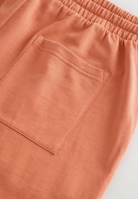 Joggers de algodón melocotón con cintura elástica y un solo bolsillo trasero, que presentan una textura limpia y suave, además de detalles de costura sutiles.