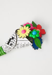 Fargerik kunstig blomsterbukett med gule, rosa, grønne og røde blomster, pakket inn i hvit papir med trykt tekst og svart rutenett-design.