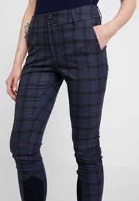 Mörkblå rutiga byxor med en strukturerad passform, med två knappar i midjan och sidofickor. Materialet har en texturerad yta.