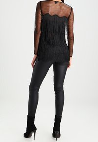 Haut noir transparent à pois avec un design à franges superposées. Associé à des leggings noirs moulants et des bottines. Texture lisse sur l'ensemble.