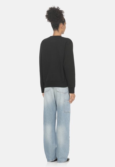 Felpa nera a maniche lunghe con scollo rotondo, abbinata a jeans a gamba larga blu chiaro con tasca laterale e finitura sbiadita.