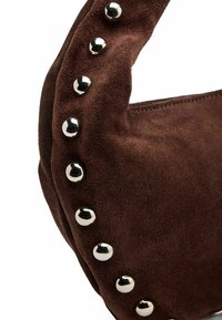 Borsa a tracolla in camoscio marrone con forma arrotondata e borchie metalliche argento lungo il bordo. Texture morbida con chiusura a cerniera.