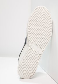 Sneaker nera con tomaia texturizzata e suola in gomma bianca con un motivo a spina di pesce. Logo impresso sul lato della suola.