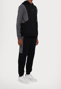 Svart och grå tvåfärgad hoodie med känguruficka, matchad med svarta sweatpants med grå sidopaneler och vita sneakers.