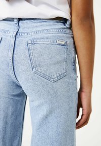 Lichtblauwe spijkerbroek met hoge taille en rechte pijpen, voorzien van een achterzak met een merkpatch en een textuurrijke afwerking.