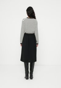 Μ αύρη midi φούστα με υφασμάτινη υφή, συνδυασμένη με μαύρο-άσπρο ριγέ μπλουζάκι μακρυμάνικο. Η μοντέλο φοράει μαύρες μπότες μέχρι το γόνατο.