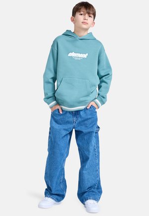 Turquoise hoodie met wit logo, kangoeroezak, gestreepte manchetten, gecombineerd met losse blauwe denim broek en witte sneakers. Casual pasvorm.