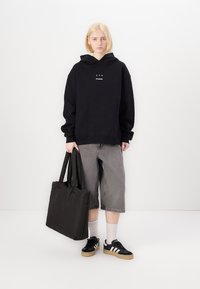 Black oversized hoodie with white logo, grey denim shorts, black tote bag, white socks, and black and white sneakers with gum sole.