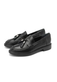 Ett par svarta läderloafers med fransdetaljer framtill och låga gummiklackar på en vit bakgrund.