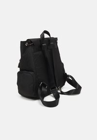Sac à dos noir en nylon de forme rectangulaire, avec des bretelles ajustables et deux poches latérales. Comprend une boucle en haut pour le transport.