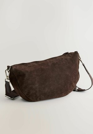 Brūns zamšs crossbody soma ar izliekto formu, ar rāvējslēdzēju augšpusē un regulējamu siksnu. Aprīkota ar sudraba toņu metāla detaļām un maigu tekstūru.