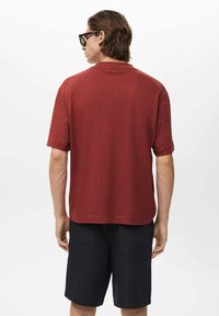 Red short-sleeve T-shirt in soft fabric, relaxed fit, and straight hem, paired with dark shorts. The design features a simple, clean look.