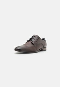 Chaussure de ville en cuir marron avec un design perforé sur la zone des orteils, lacets ronds et un petit talon. Finition lisse avec une pointe contrastante plus sombre.