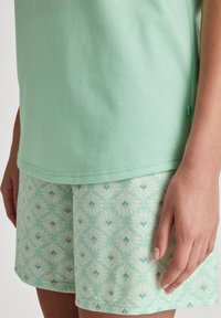 Mintgrünes Baumwoll-T-Shirt kombiniert mit mintgrün gemusterten Shorts im Blumenmotiv, mit einer weichen Textur und einem entspannten Schnitt.