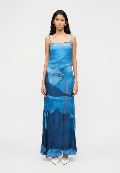 Robe longue bleue à fines bretelles, présentant un motif aquarelle de vagues et de nuages. Confectionnée en tissu léger et transparent.