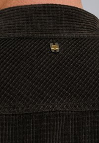 Camisa de pana oscura con textura de ribetes verticales, diseño con cuello y una etiqueta dorada con el logo "PME LEGEND".